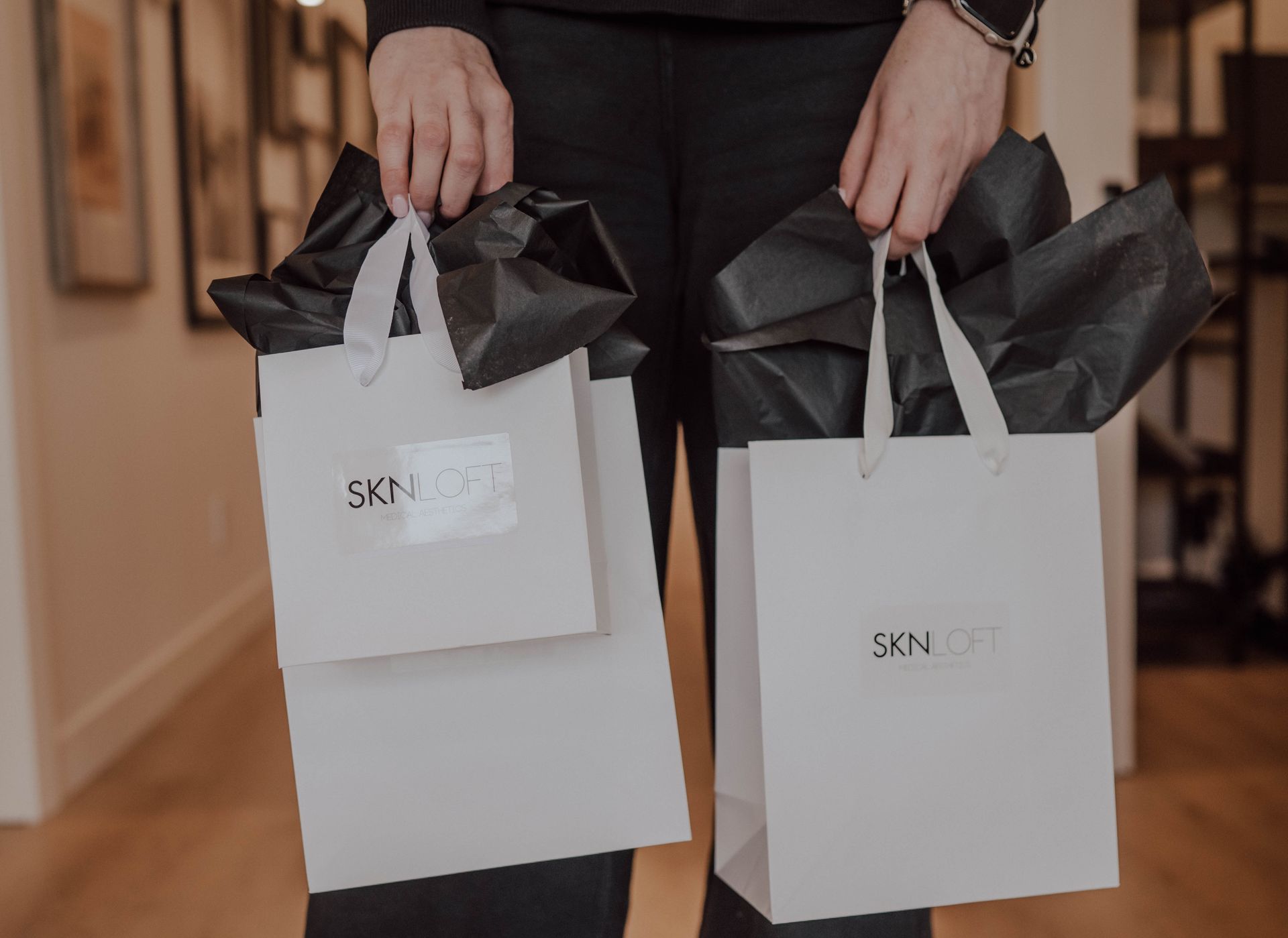 Person holding two white SKN LOFT shopping bags with black tissue paper.