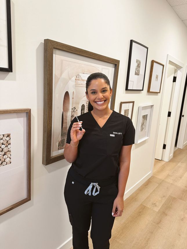 A woman is standing in a hallway holding a syringe and smiling.