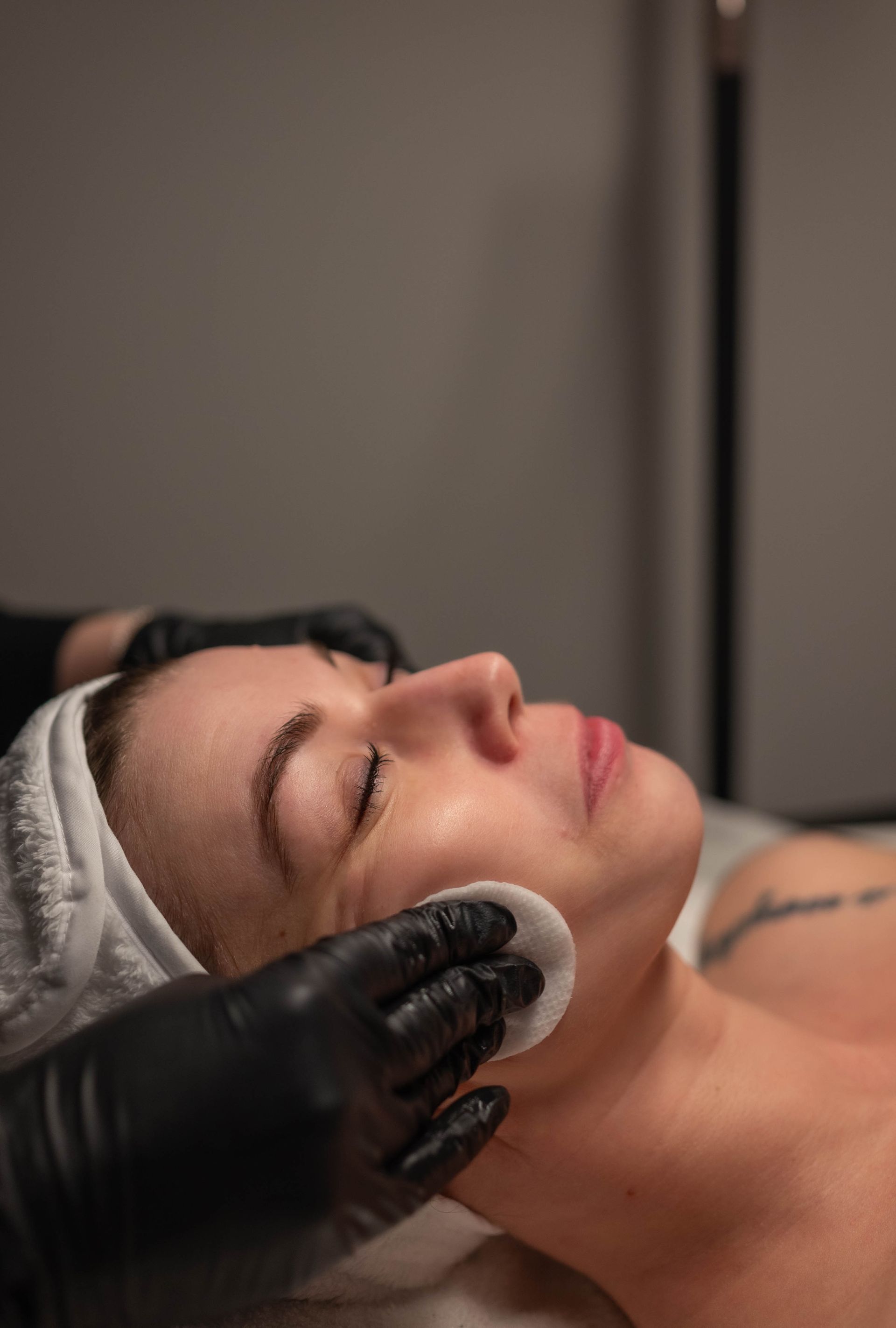 Woman receiving facial treatment; cotton pad cleanses her face.