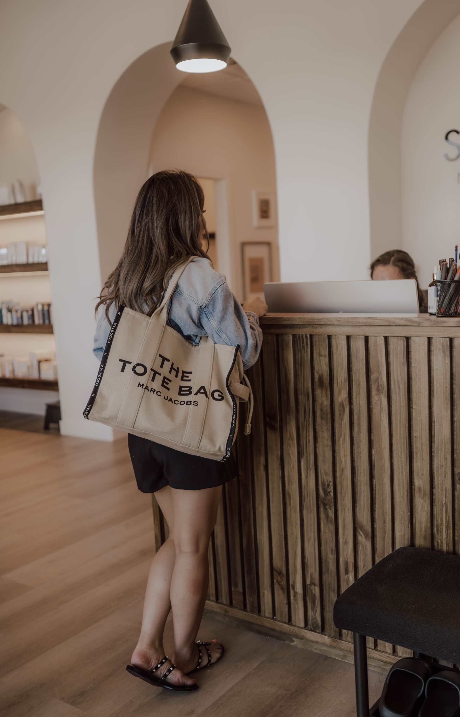 A woman is standing at a counter in a store holding a tote bag.