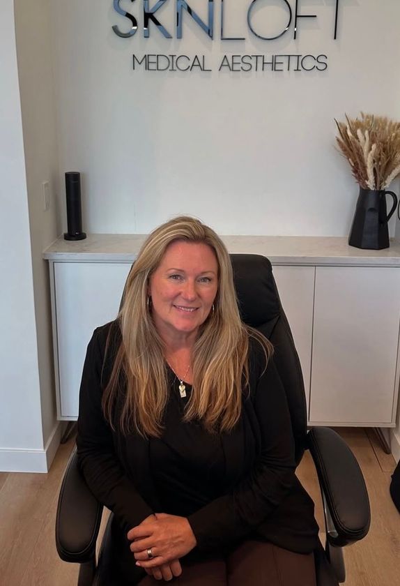 A woman is sitting in a chair in front of a sign that says skinloft medical aesthetics