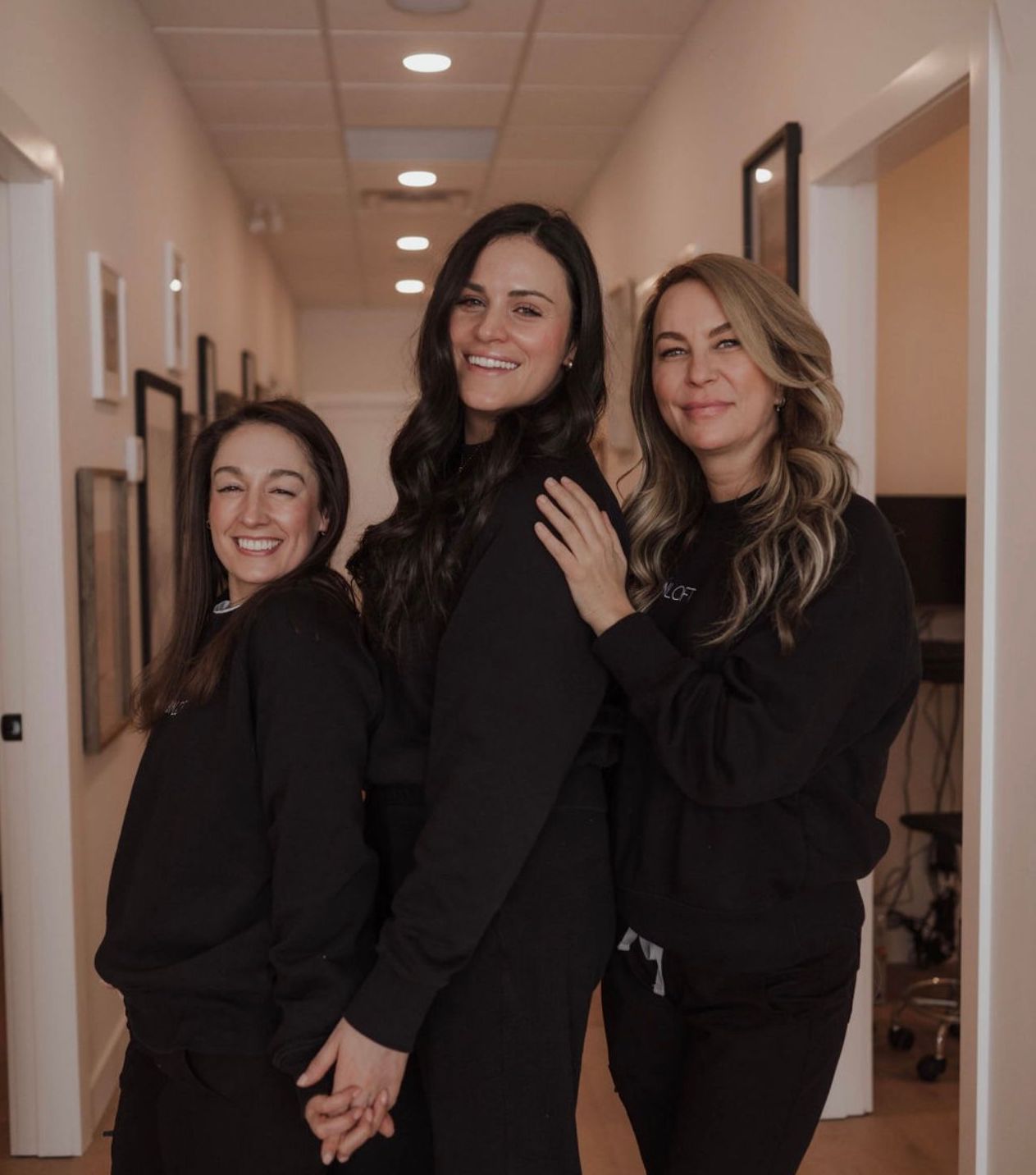 three women in black sweatshirts are posing for a picture in a hallway