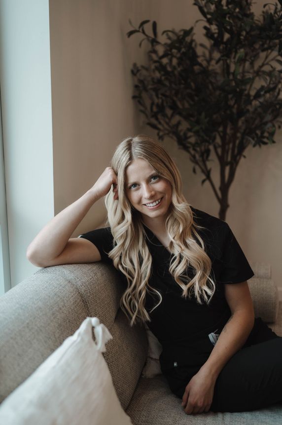 A woman is sitting on a couch with her hand on her head.