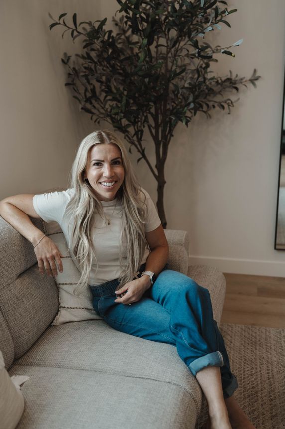 A woman is sitting on a couch in front of a tree.