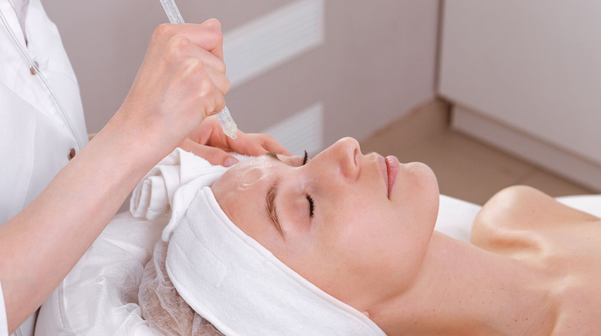 Woman receiving a facial treatment in a spa, with a technician using a device on her face.