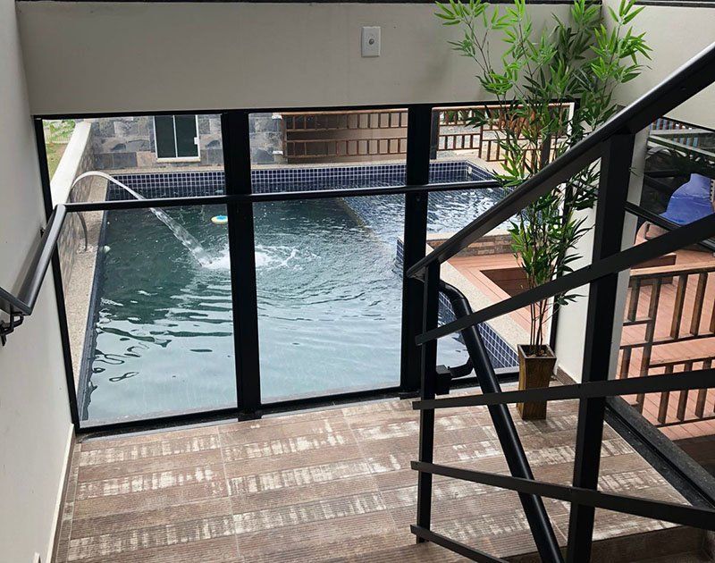 Escadas com vista através de uma grande janela de vidro para uma piscina com fonte e uma planta de interior.