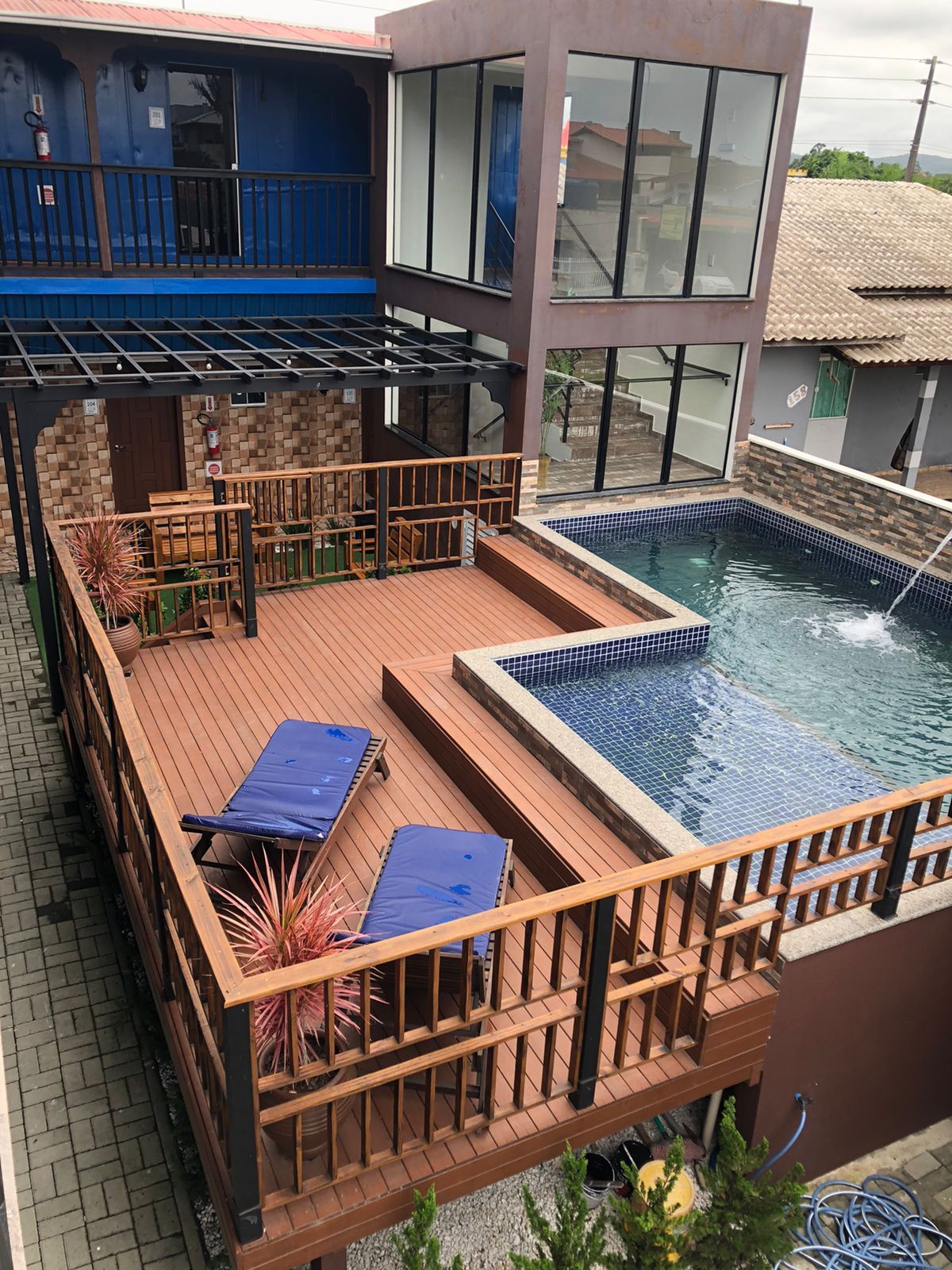 Deck de madeira elevado com duas espreguiçadeiras azuis ao lado de uma piscina em forma de L junto a um edifício moderno.