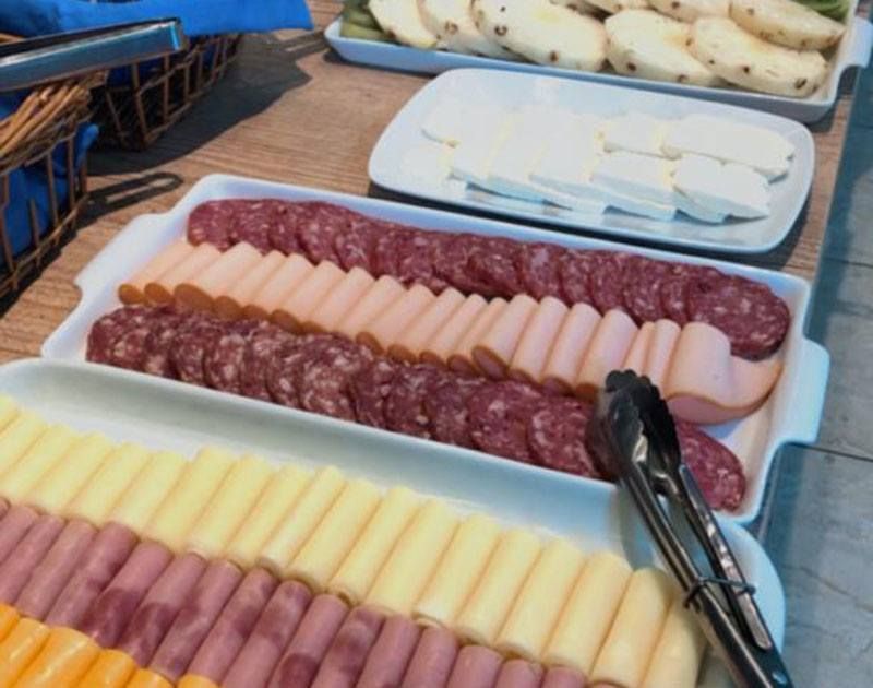 Um buffet de café da manhã com travessas de frios, queijos e frutas dispostas sobre uma mesa.