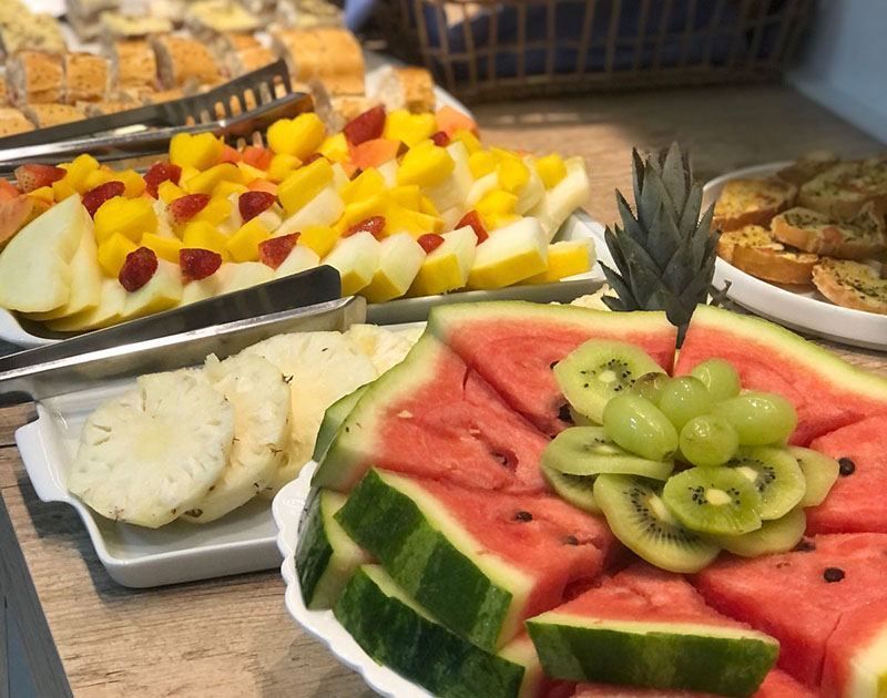 Uma variedade de frutas frescas, incluindo melancia, abacaxi, kiwi e uvas, dispostas em travessas em um bufê.