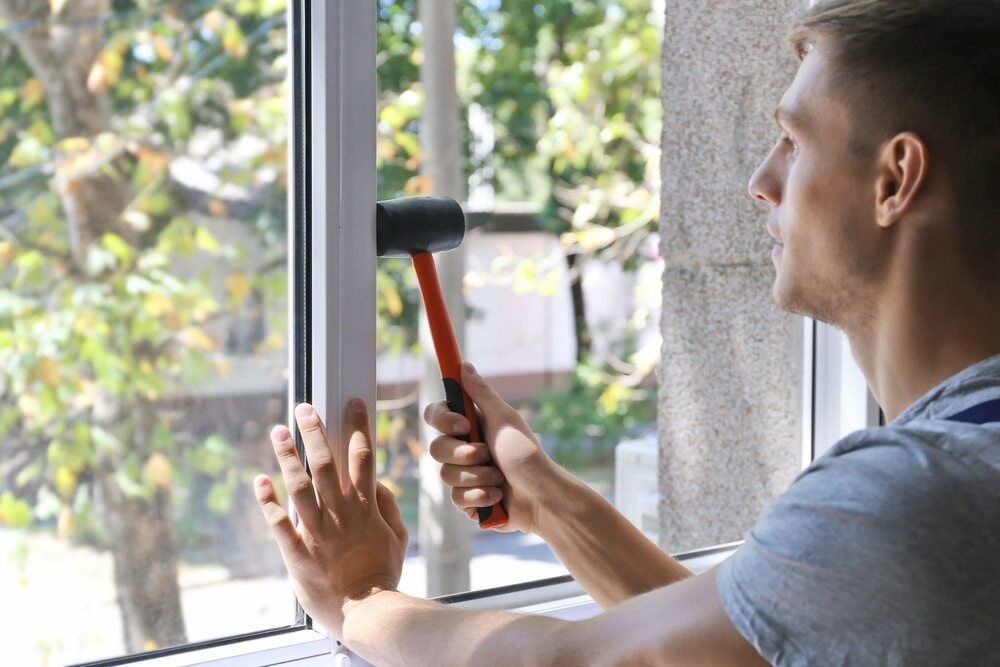 A Man is Using a Hammer to Fix a Window — Bulli Glass in Bulli, NSW