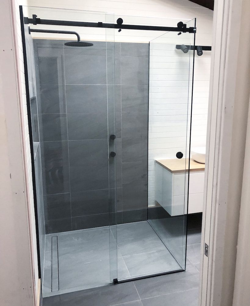 A Bathroom with a Sliding Glass Shower Door and a Black Shower Head — Bulli Glass in Bulli, NSW
