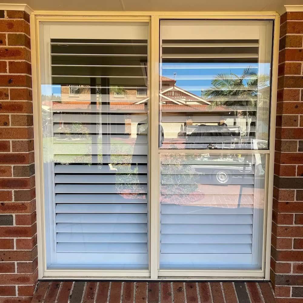 A Sliding Glass Door with Shutters on It and a Brick Wall Behind It — Bulli Glass in Bulli, NSW