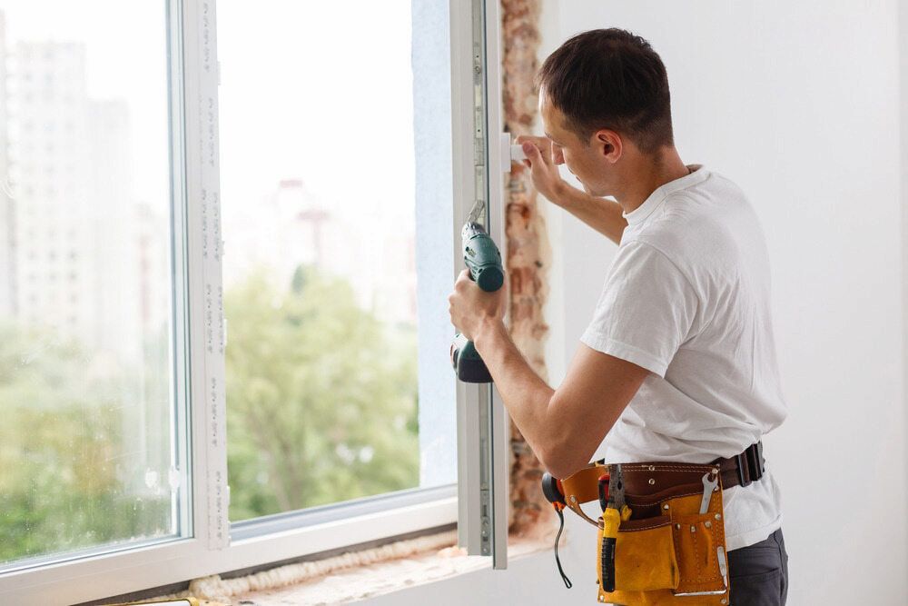 A Man is Installing a Window with a Drill — Bulli Glass in Bulli, NSW