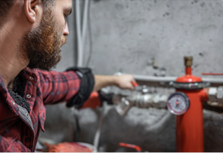Man in plaid shirt adjusts a valve on red pipe system in an industrial setting.