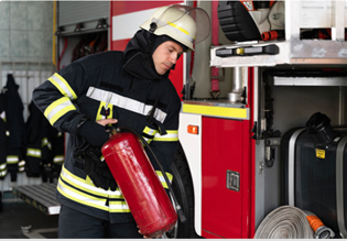 Firefighter holding a red fire extinguisher near a fire truck, preparing for action.
