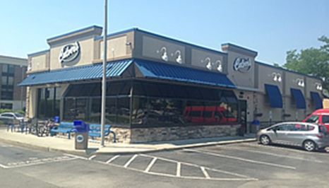 Exterior of an Arby's restaurant with blue awnings, a stone facade, and a parking lot.