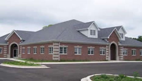 Red brick commercial building with gray roof and dormers. Black asphalt parking lot.