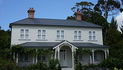 Two-story white house with dark roof and porch, surrounded by greenery.