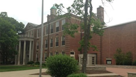 Brick building with columns and a green dome, trees, and a concrete path.