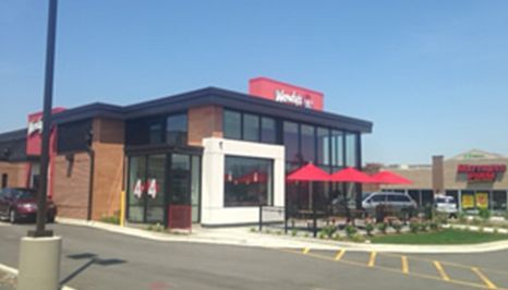 Exterior of a Wendy's restaurant in daylight, with red umbrellas and parking spaces visible.
