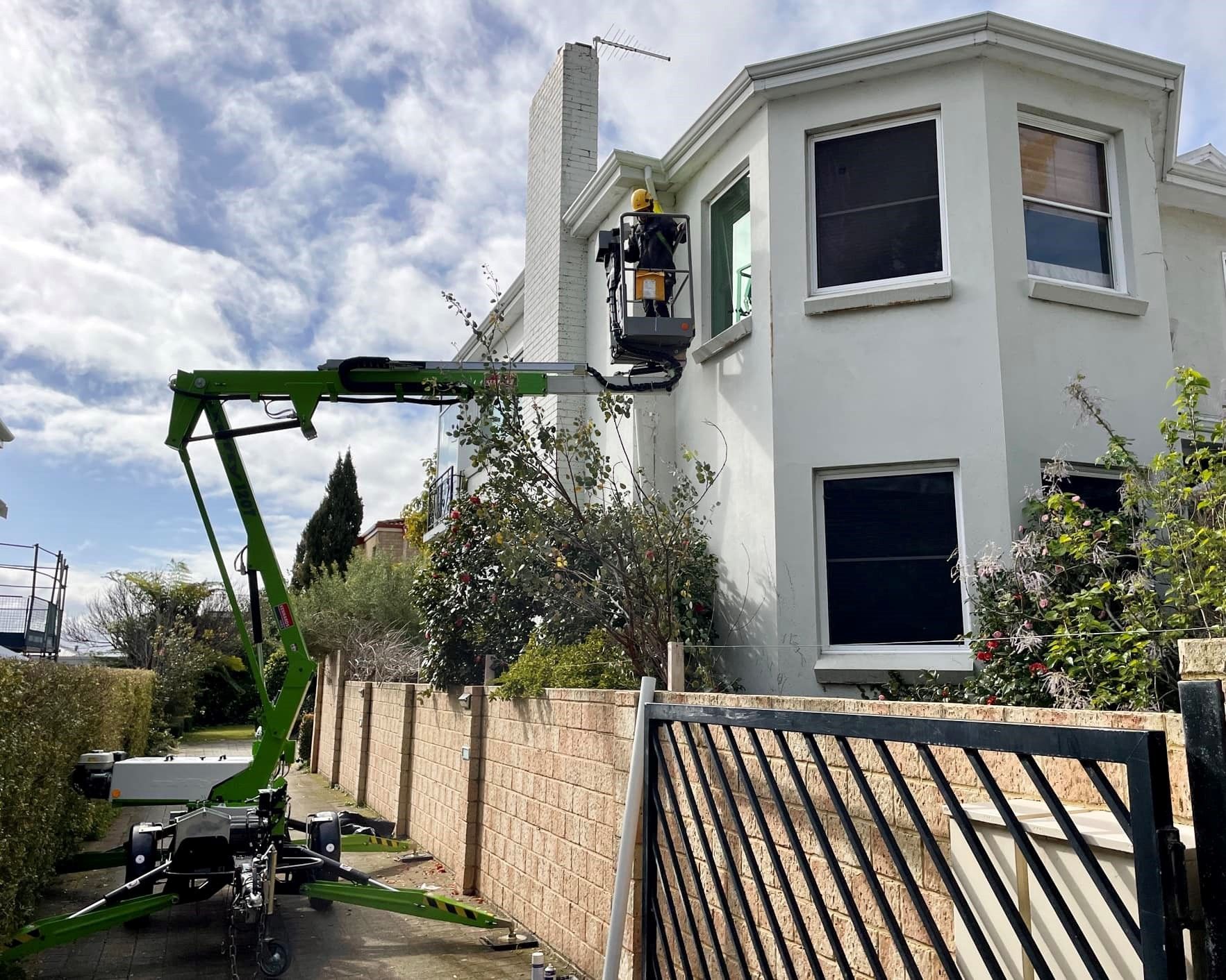 Gutter Installation Image a green crane is sitting in front of a white house .