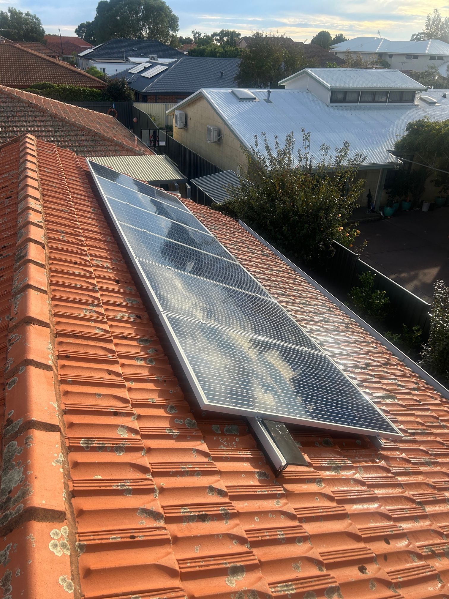 A solar panel is sitting on top of a tiled roof.