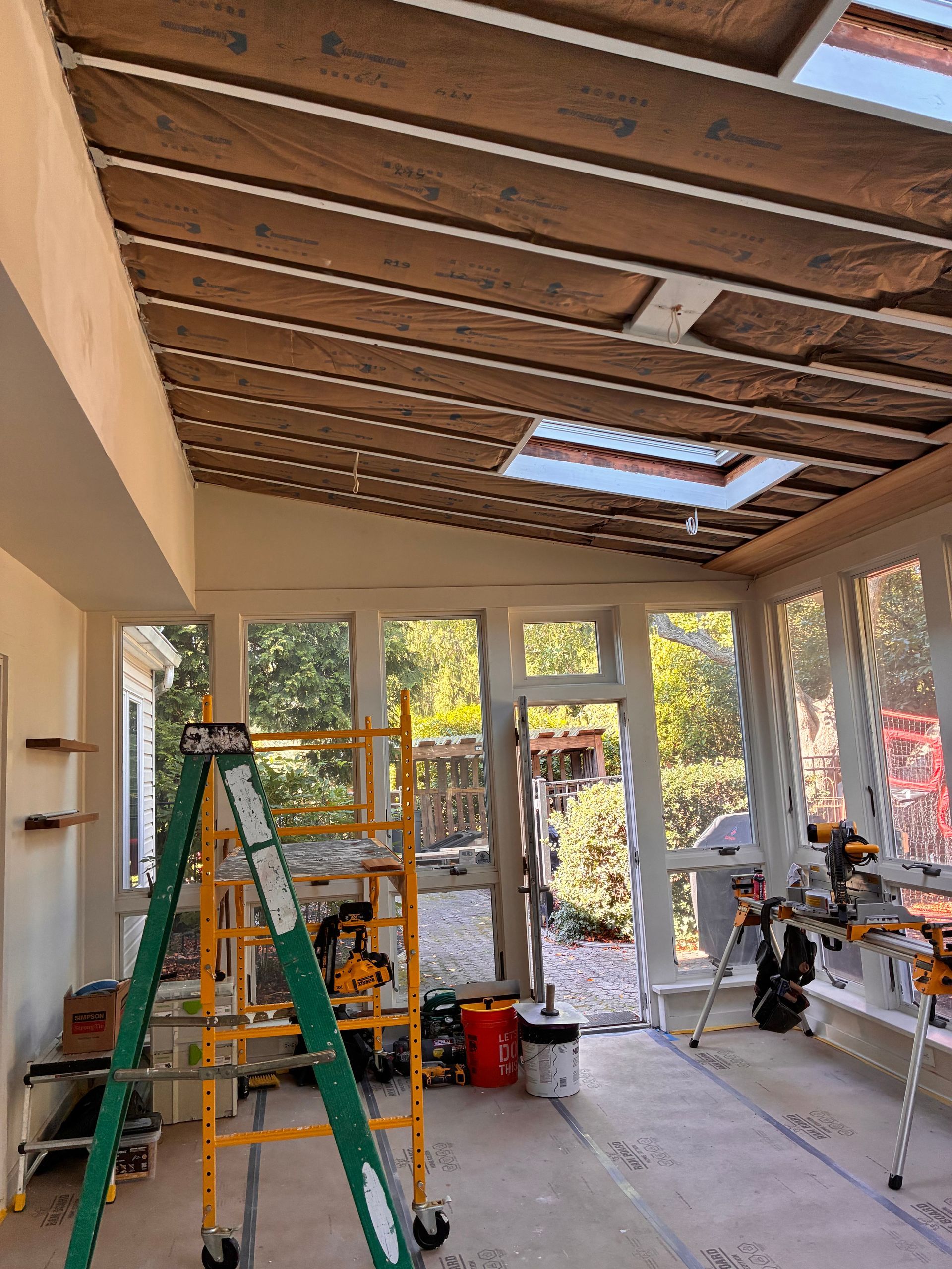 Sunroom under construction, showing insulation in the ceiling, skylights, and tools scattered throughout.