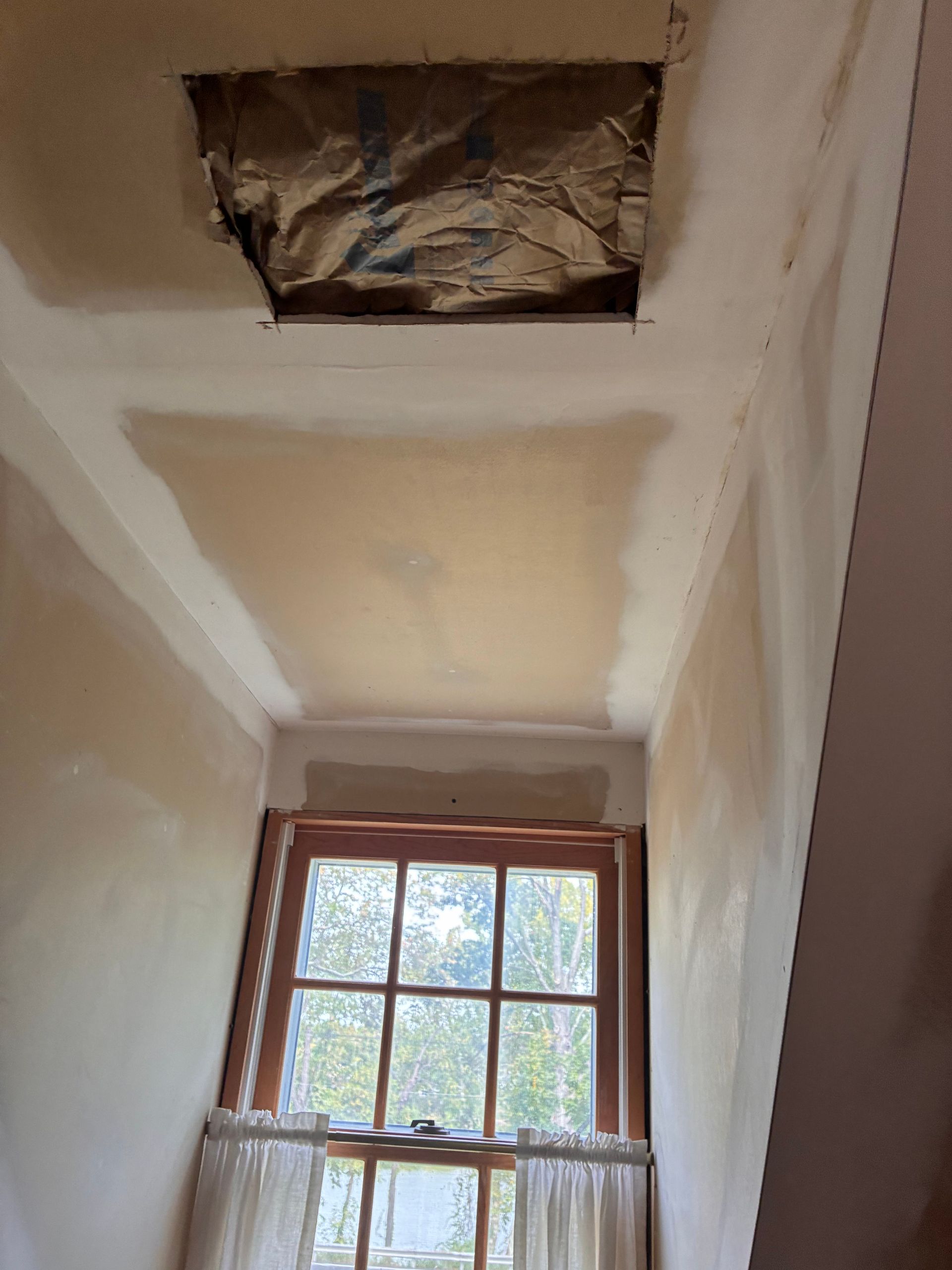 Ceiling with a window and a square opening covered in foil. Partially plastered.