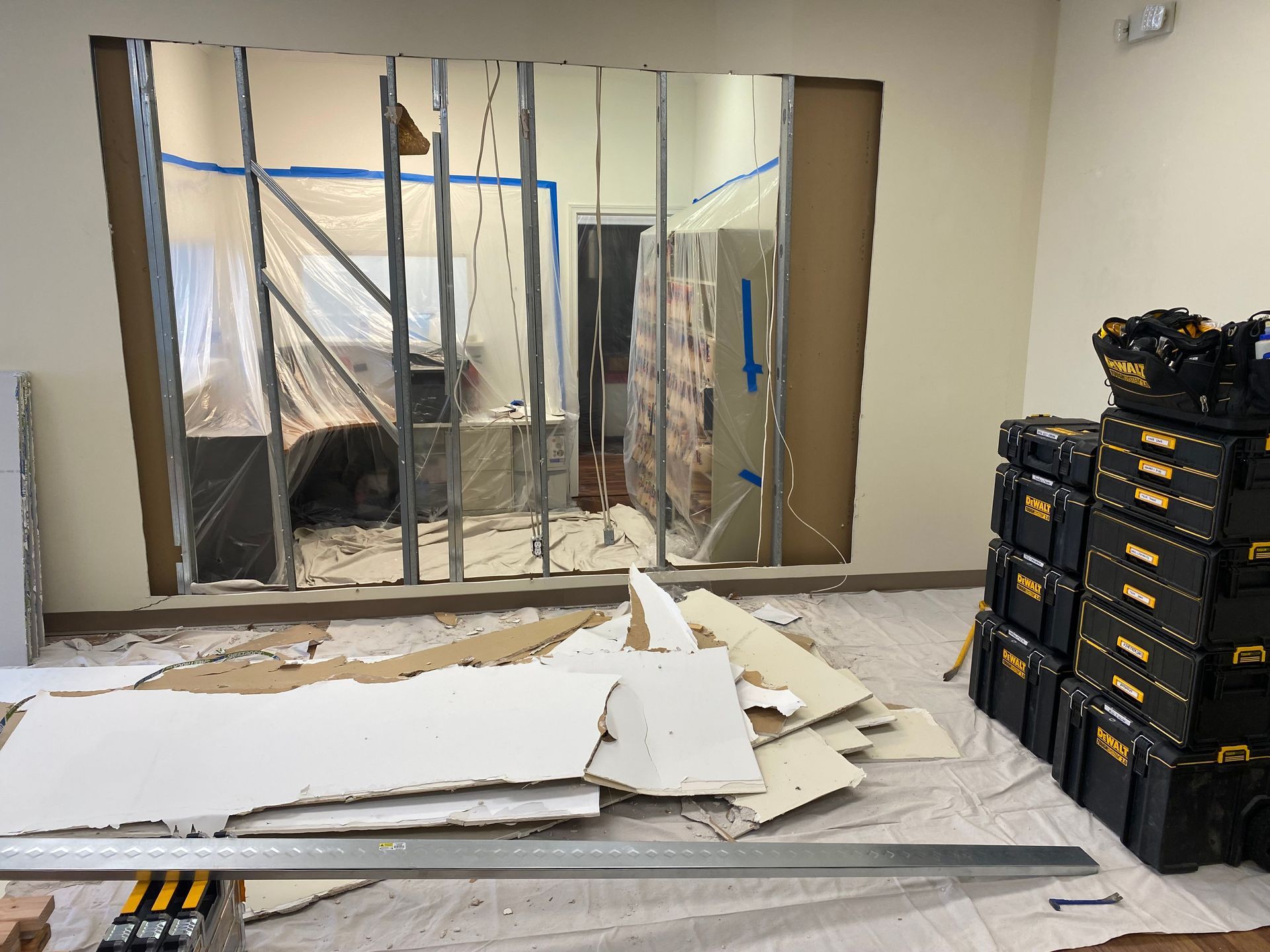 Room renovation: A wall is open, exposing metal studs. Debris and tools are on the floor.