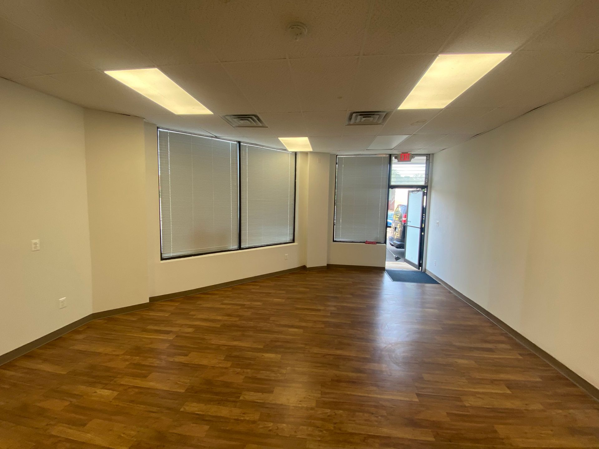 Empty retail space with hardwood floors, windows, and an open doorway.