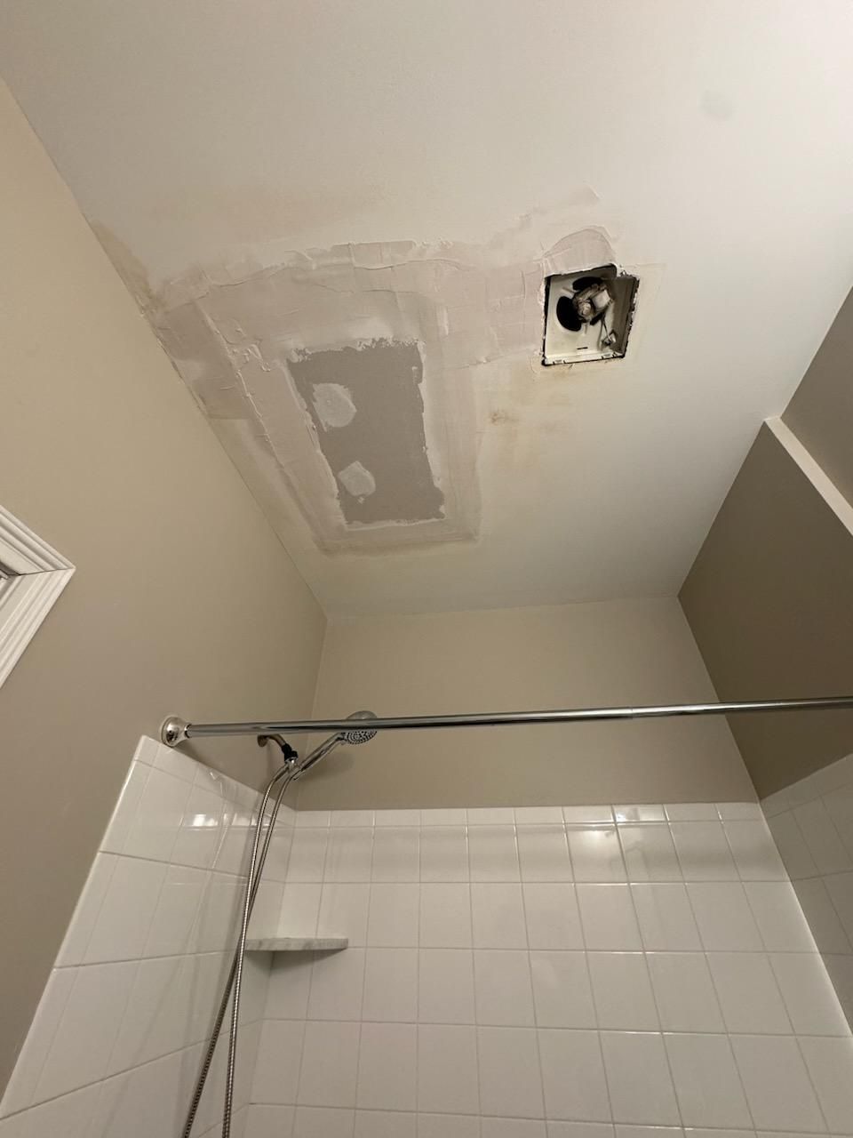 Bathroom ceiling with patched holes above a shower.