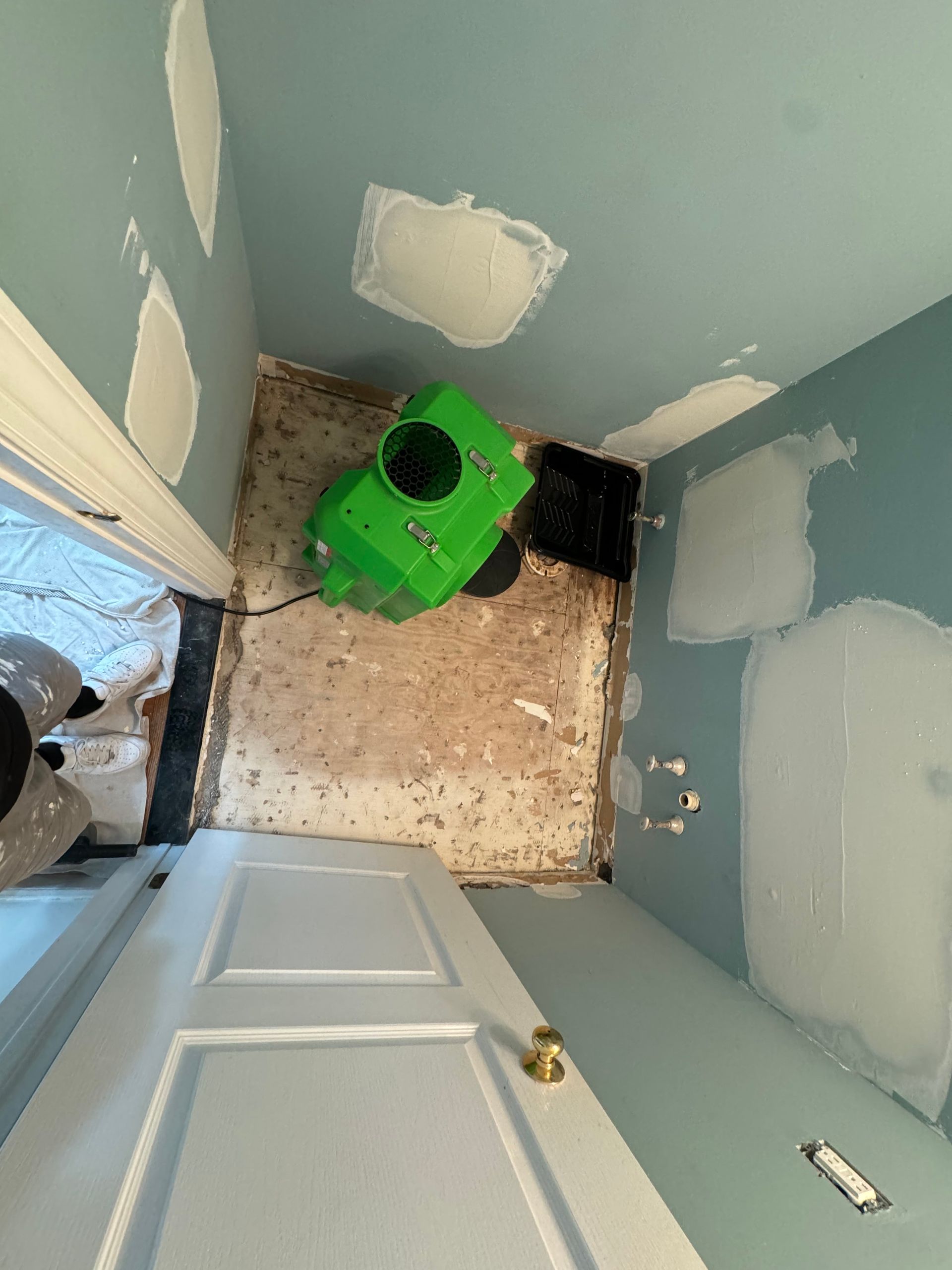 Green dehumidifier in a small room with blue walls and patched drywall. A white door is in the foreground.