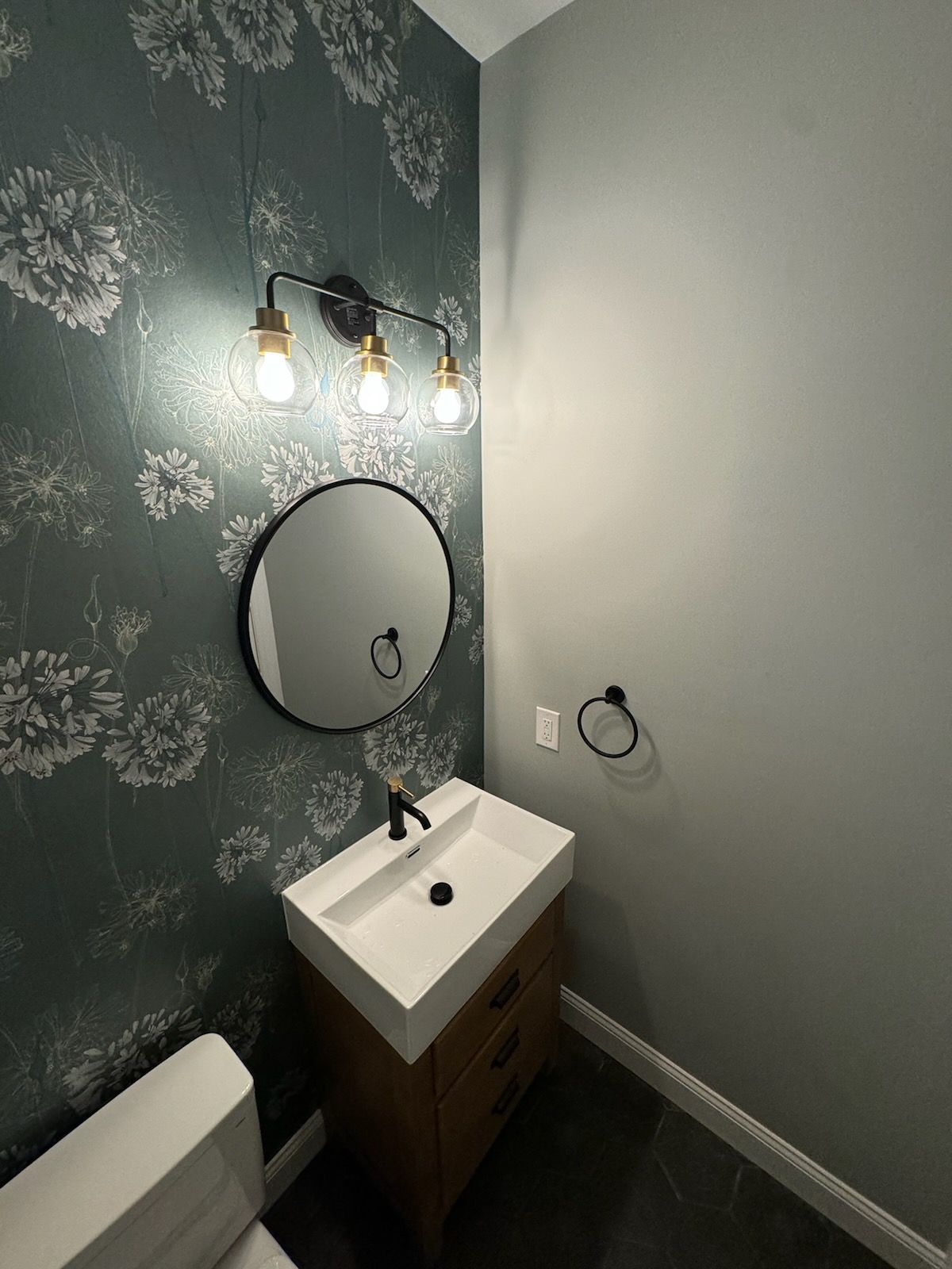 A small bathroom with floral wallpaper, a black-framed mirror, and a modern sink.