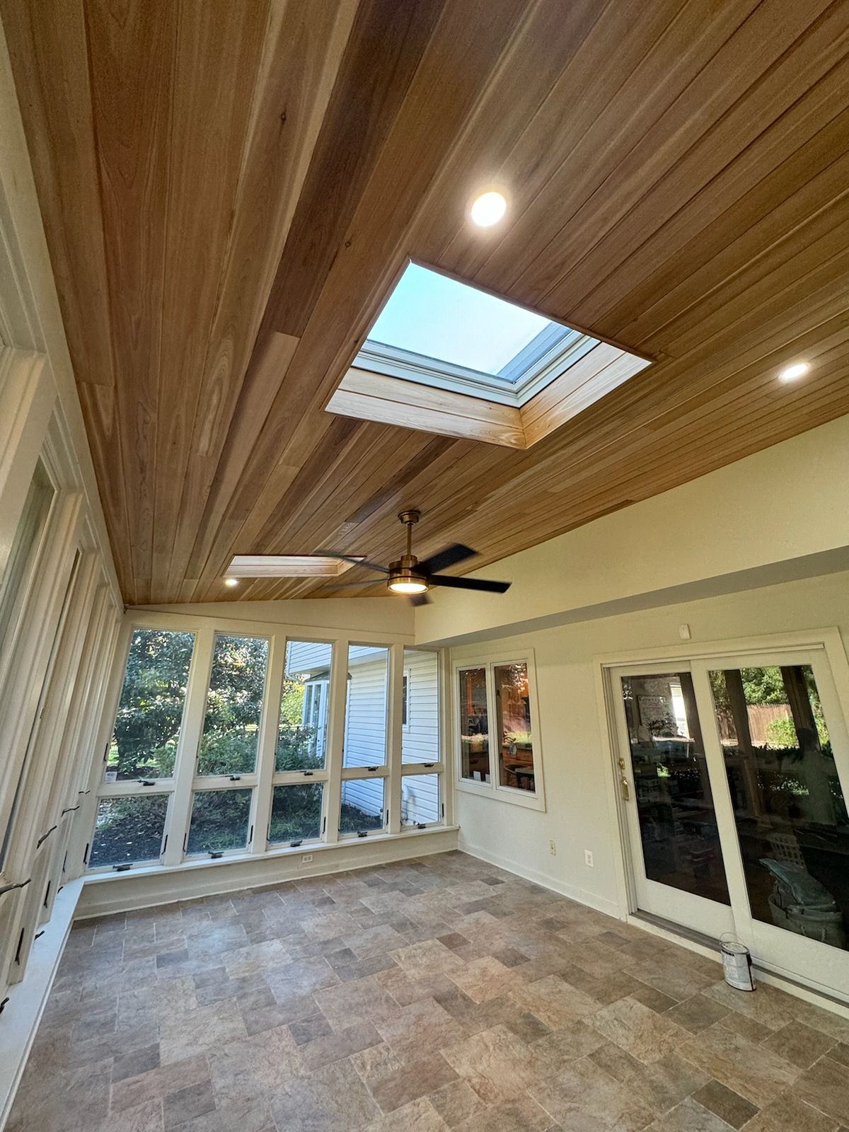 Sunroom interior with wood ceiling, skylights, and tile floor.