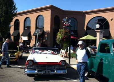 A man is walking in front of a building with cars parked in front of it