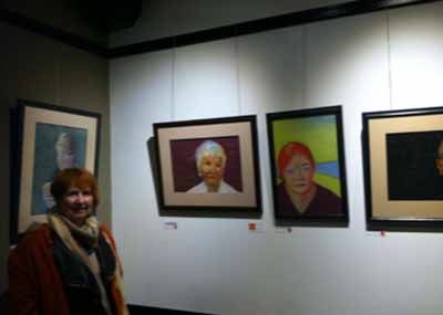 A woman is standing in front of a wall with paintings on it.