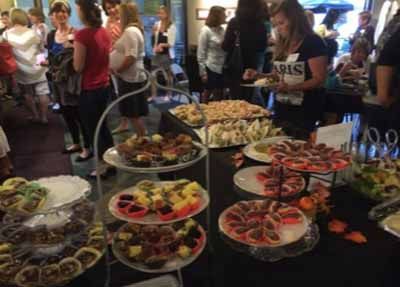 A group of people are standing around a table with plates of food on it.