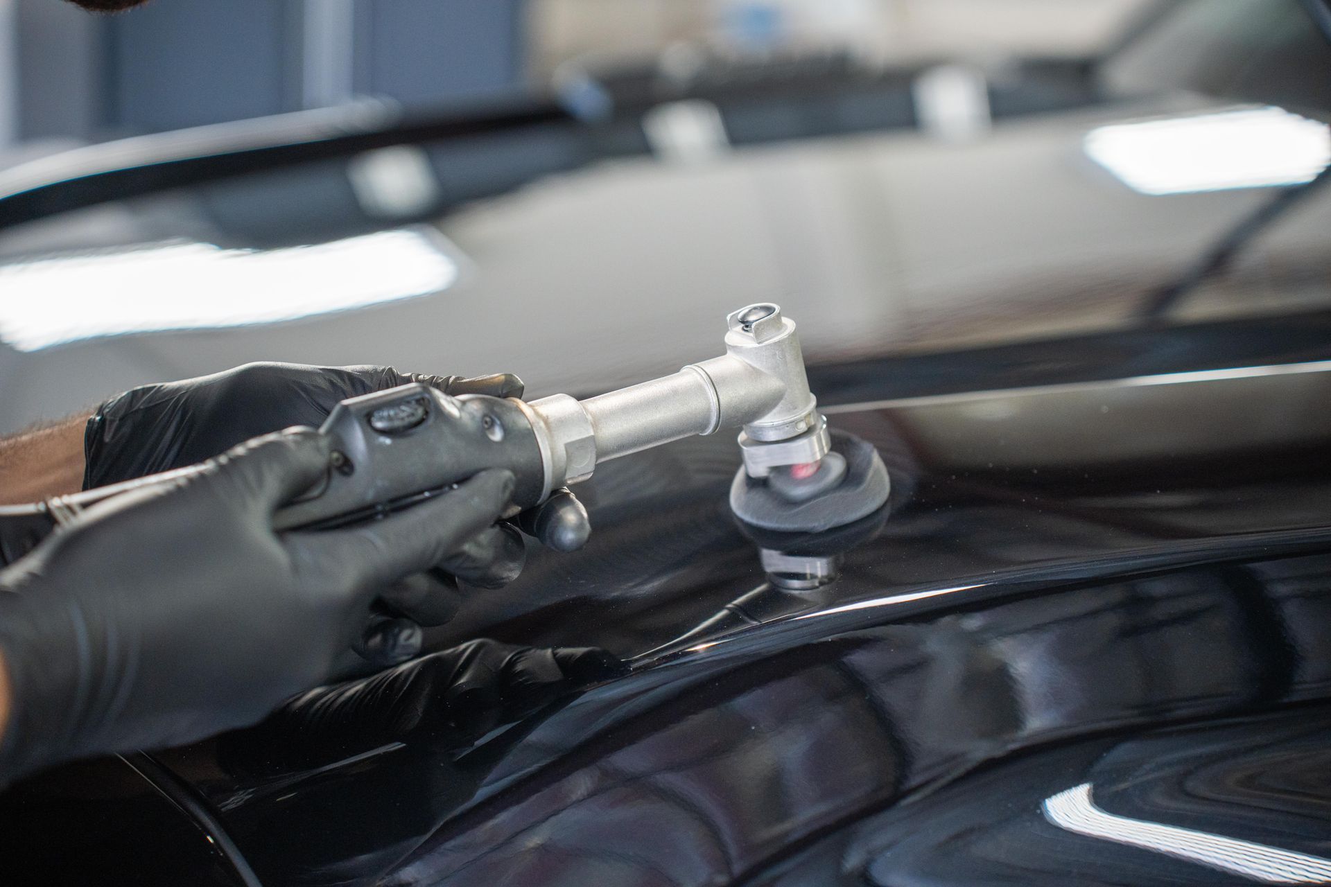 Person wearing black gloves polishing a black car with a rotary tool.