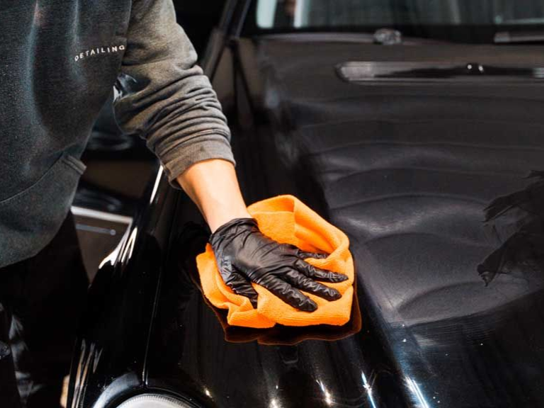 Black-gloved hands using a polisher on a black car panel. Detailing and shining a vehicle.