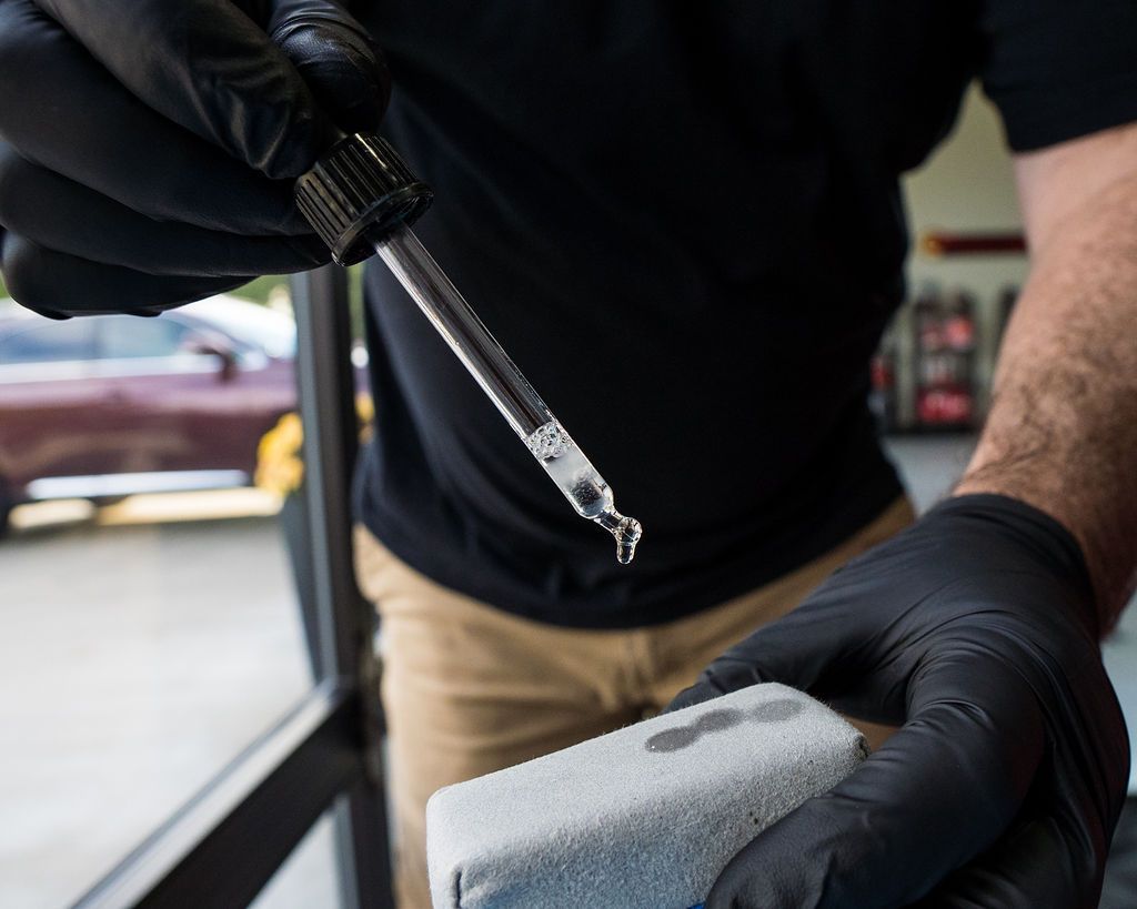 Person in black gloves applying a detailing product to a red car in a well-lit garage.