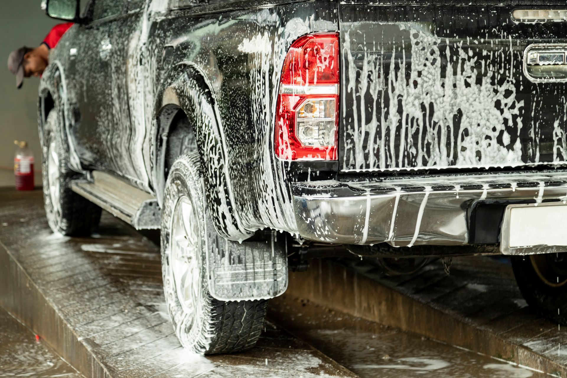 Black pickup truck being washed with soap at a car wash.