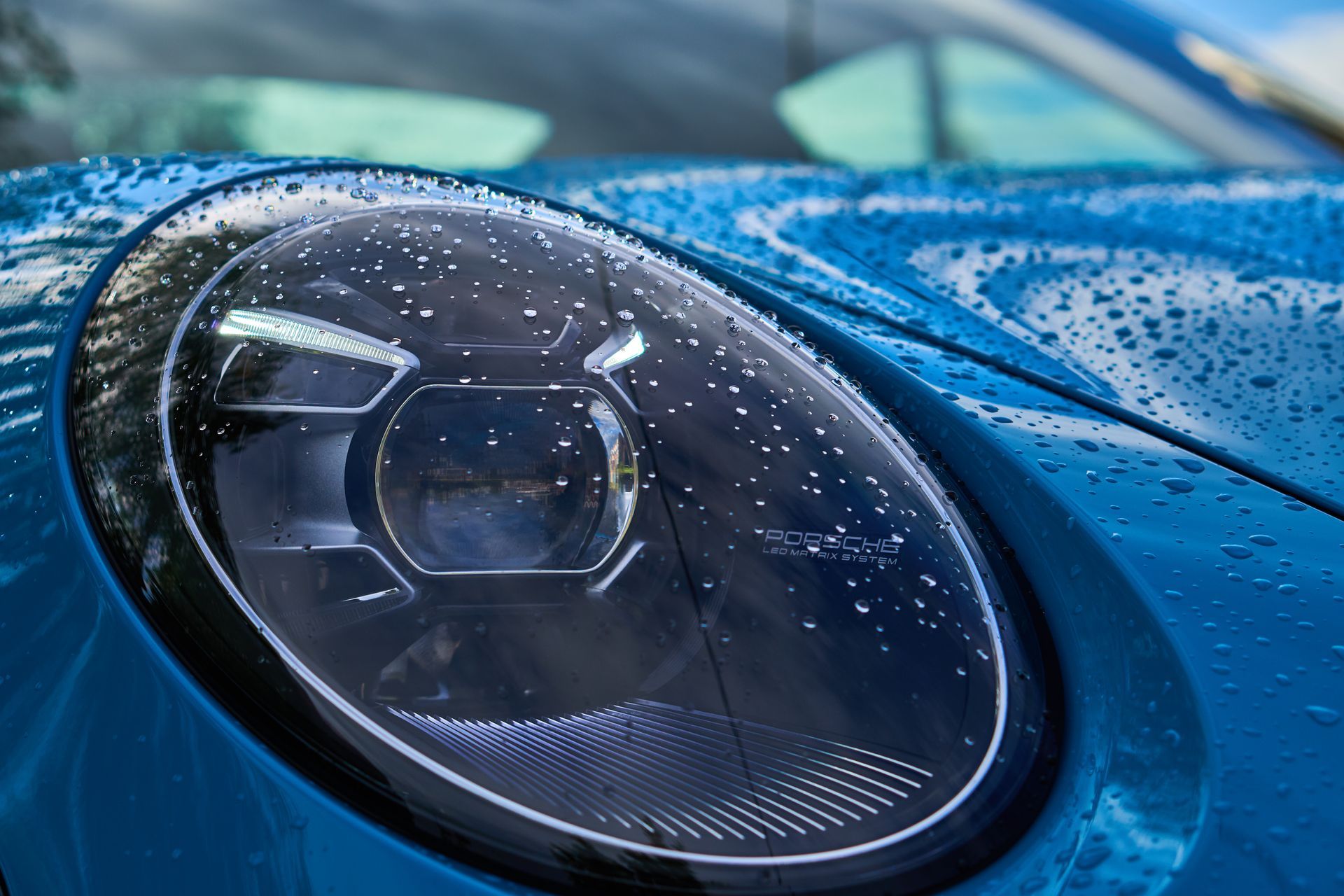 Blue Porsche headlight with water droplets.