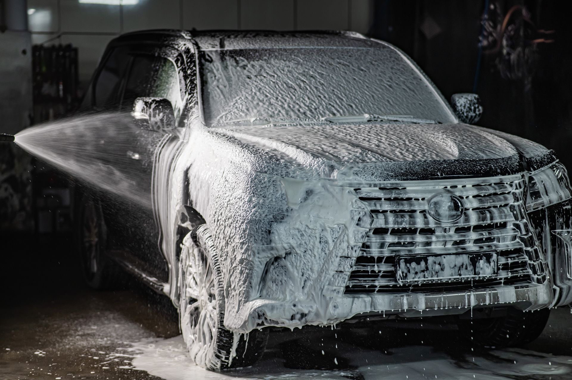 Black pickup truck covered in white foam at a car wash.