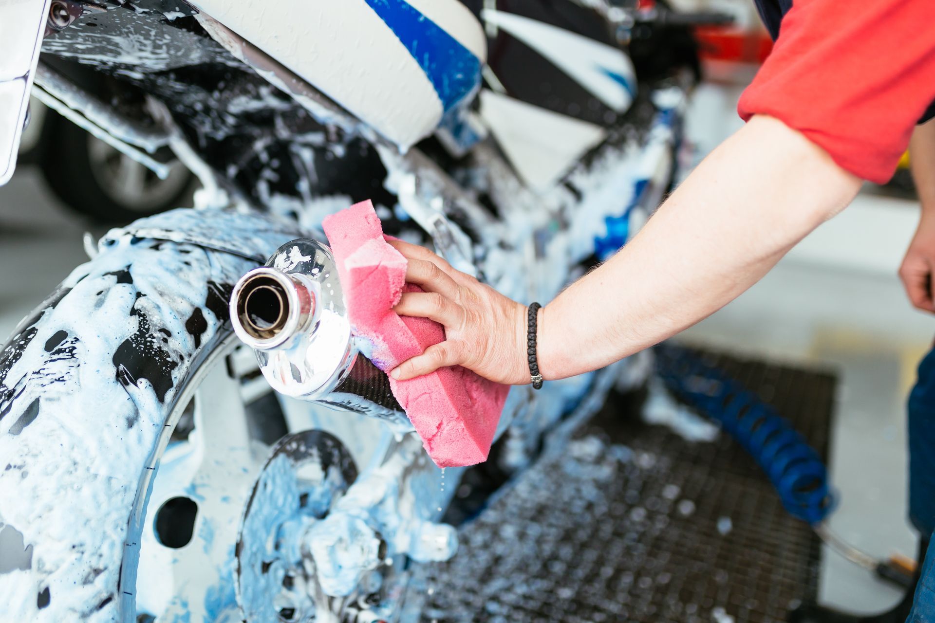 Person washing a motorcycle with a sponge, covered in soap, outdoors.