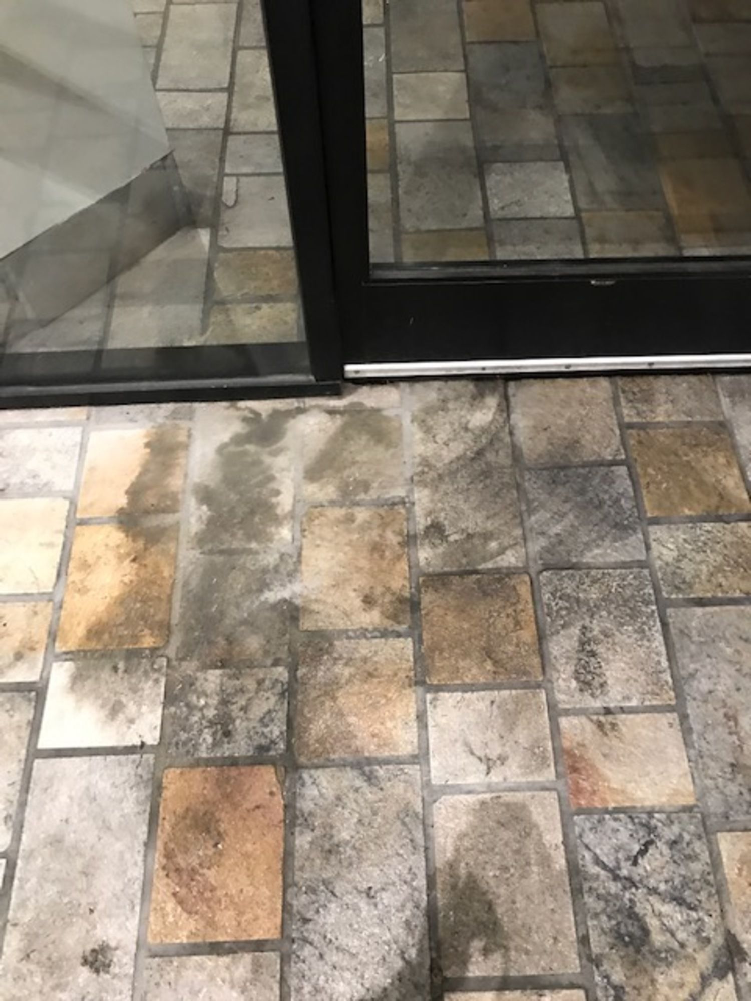 A dirty tile floor next to a glass door.