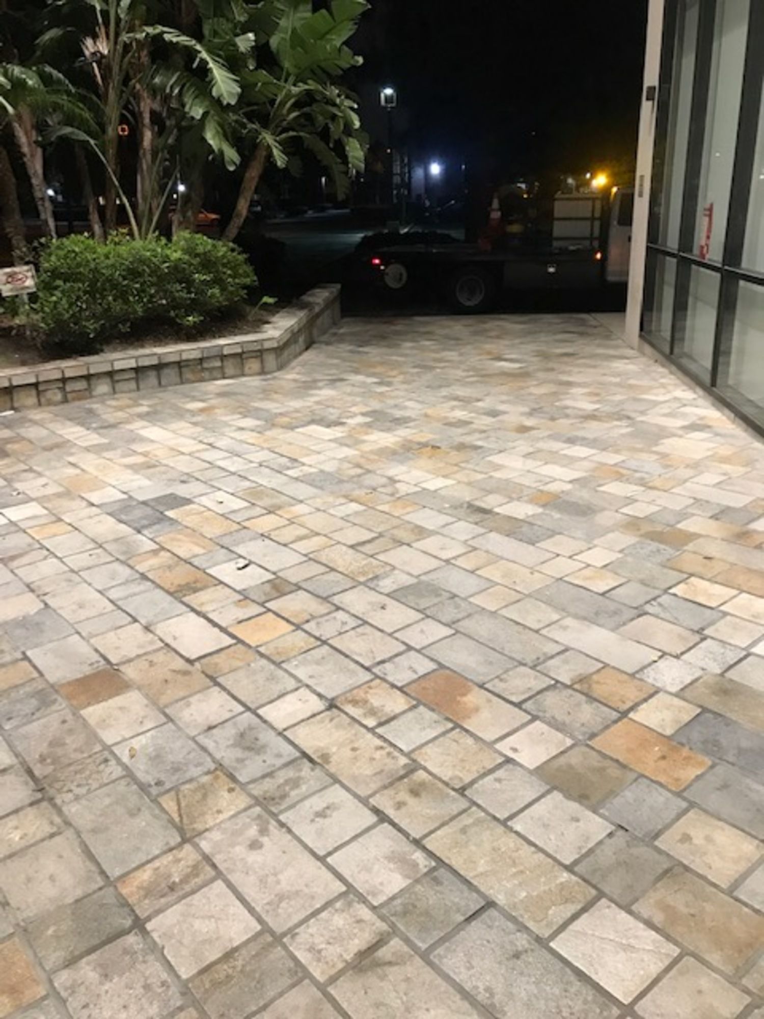 A brick patio with a car parked in the background at night.