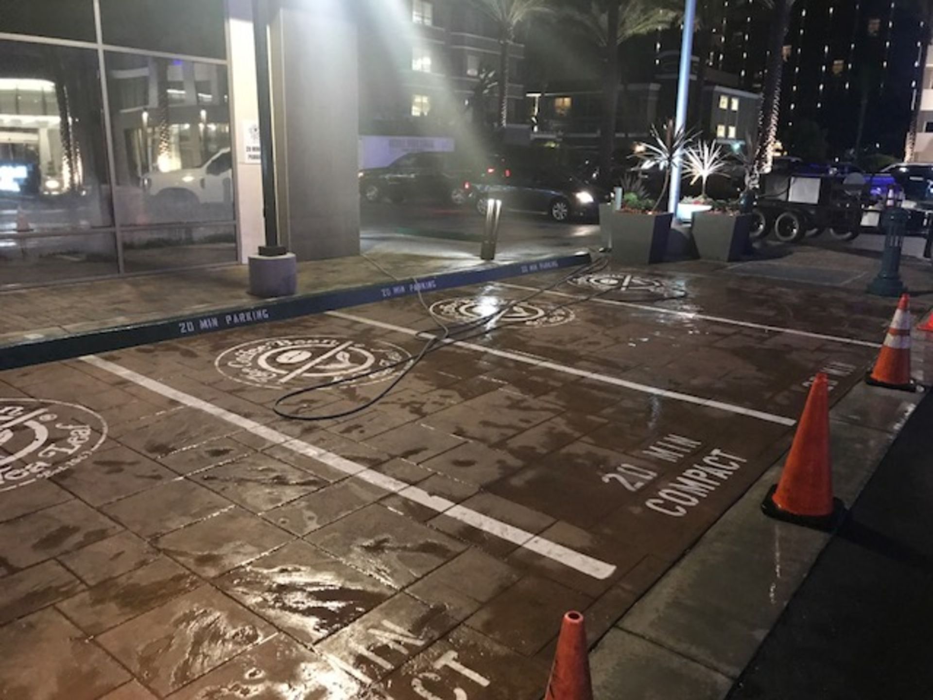 A parking lot is being cleaned at night with a hose and cones.
