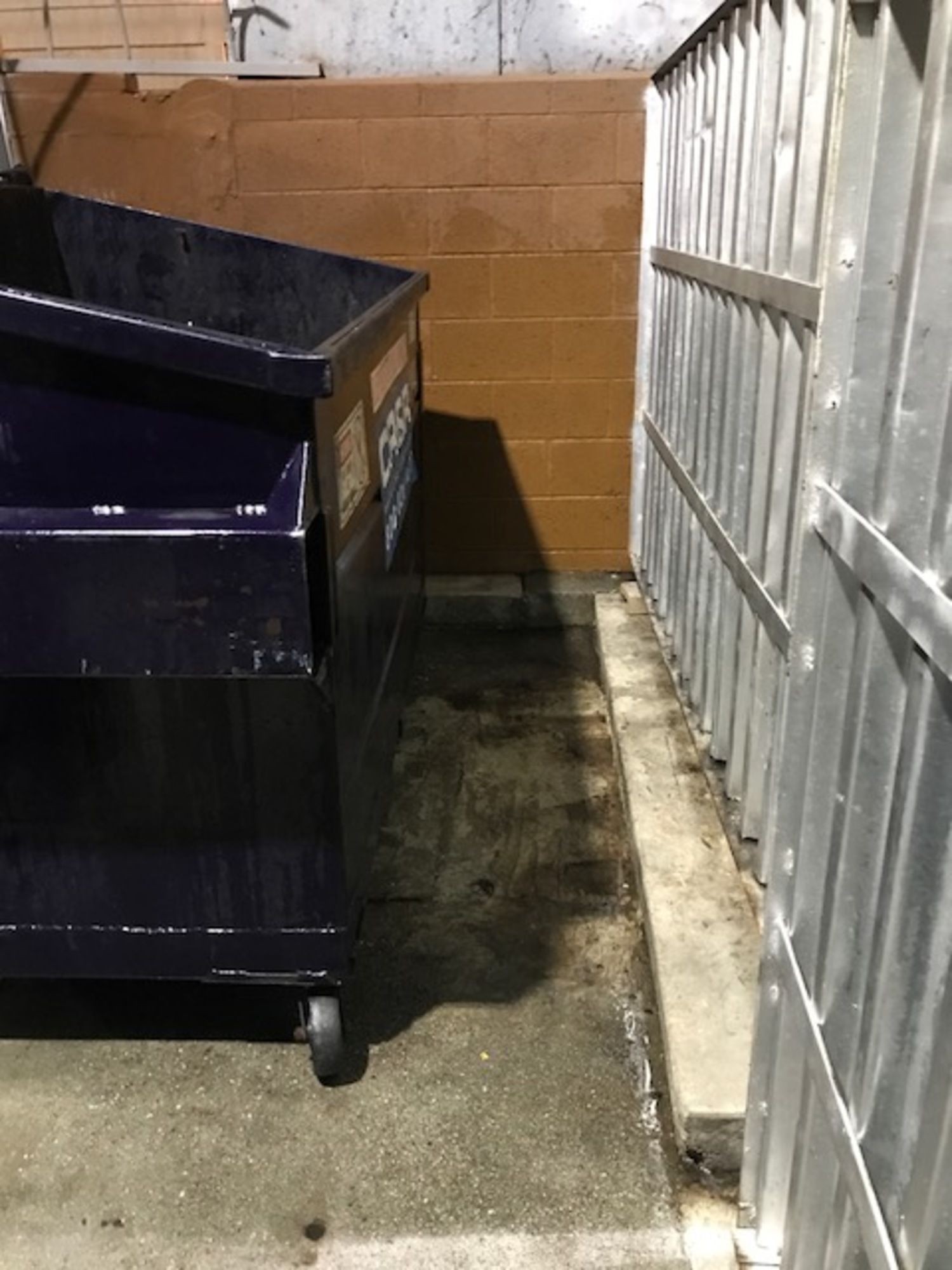 A dumpster is sitting next to a fence in a parking lot.