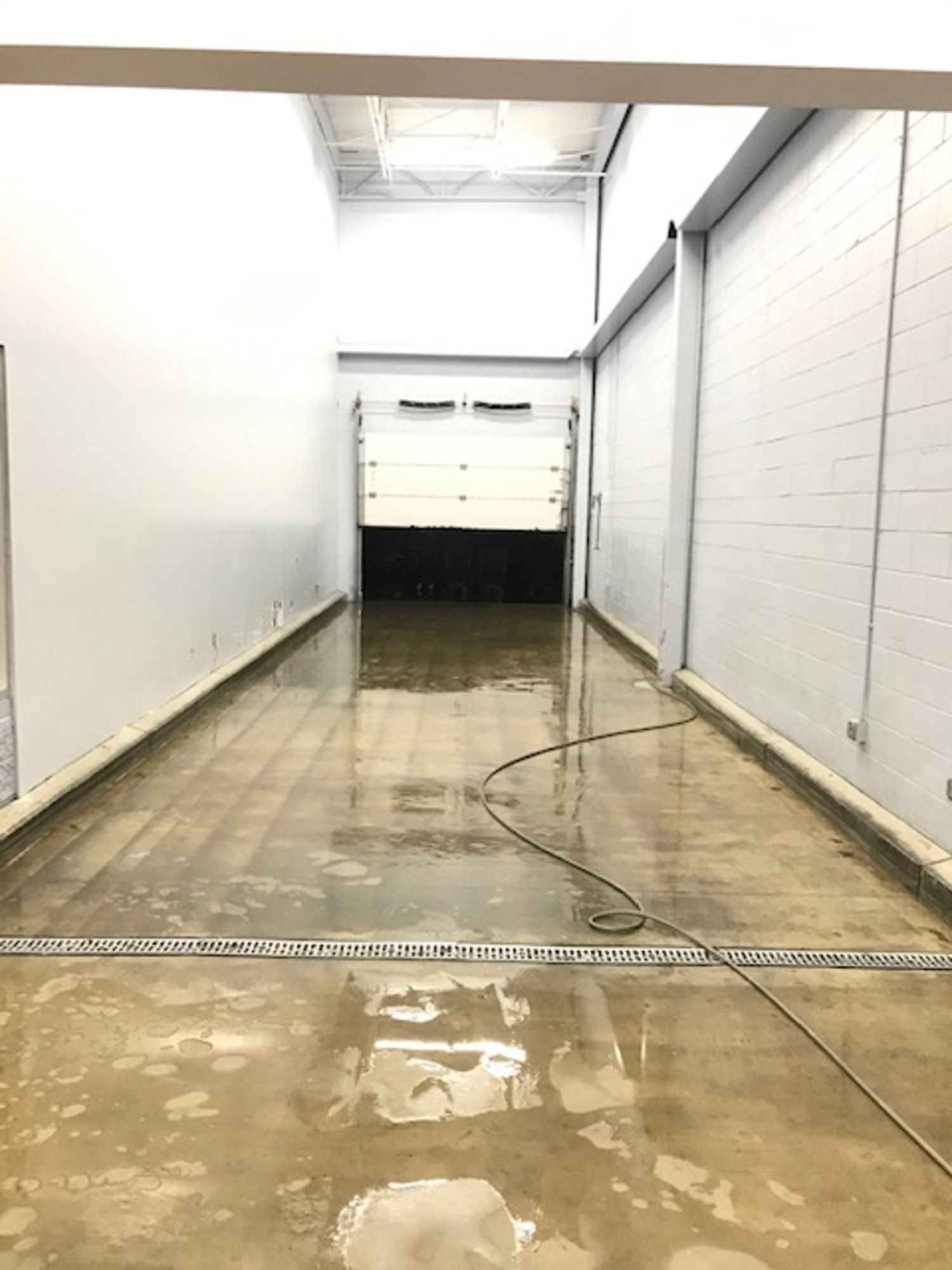A long hallway with a drain in the middle of it leading to a garage door.