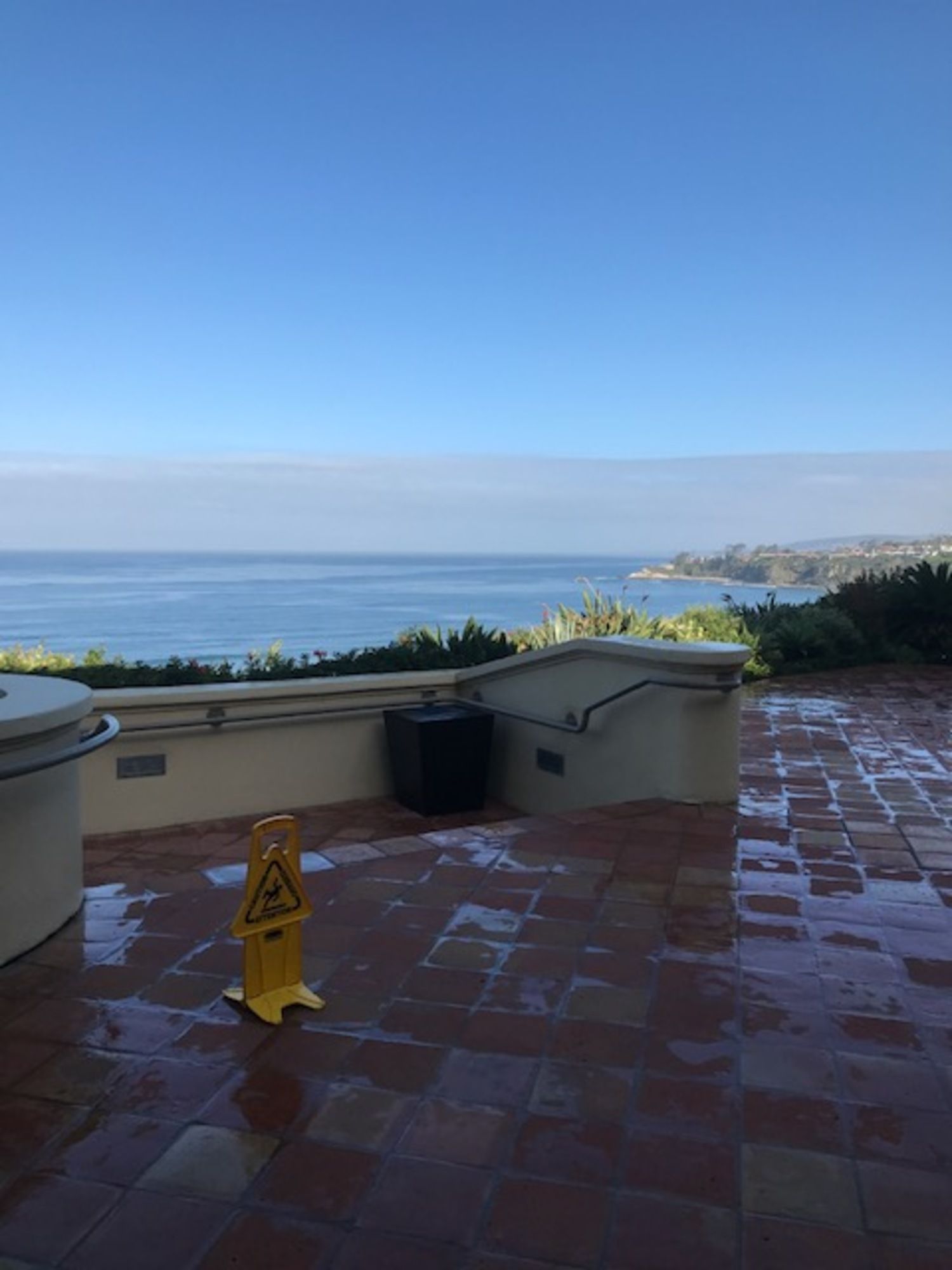 A yellow caution sign sits on a tiled floor overlooking the ocean.